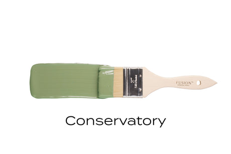 Paintbrush with mid-tone green bristles and “Conservatory Fusion Mineral Paint” text below by Fusion Mineral Paint.