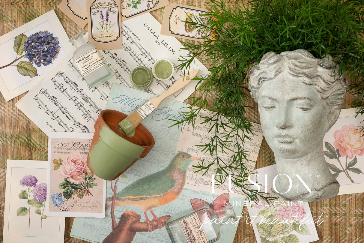 Conservatory Fusion Mineral Paint with art supplies, vintage postcards, plant, and stone bust on woven surface.