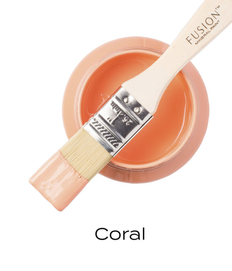 Paintbrush on open jar of Coral Fusion Mineral Paint (Seasonal), matte coral color visible below.