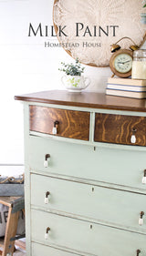 Vintage dresser painted with Homestead House Craftsman Milk Paint, with two dark wood drawers, books, and a clock on top.