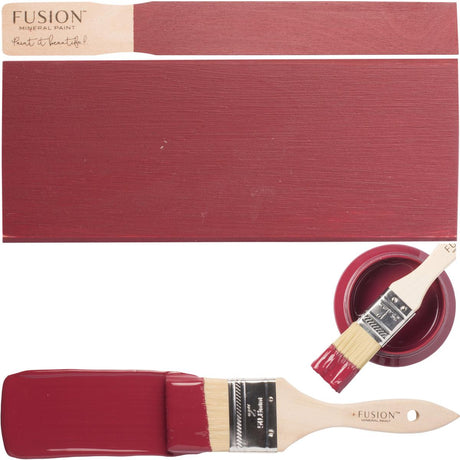 Paintbrush with Cranberry Fusion Mineral Paint, color swatches, and Fusion Mineral Paint container labeled “Fusion.”.