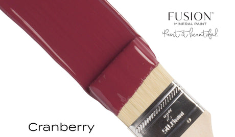 Paintbrush dipped in Cranberry Fusion Mineral Paint, a rich burgundy red by Fusion Mineral Paint.
