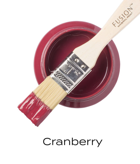 Open can of Fusion Mineral Paint in deep red Cranberry Fusion, brush dipped in, label visible underneath.