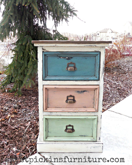 Small dresser in Creamy by Old Fashioned Milk Paint with blue, pink, and green drawers and brass handles.