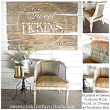 Rustic chair with burlap upholstery next to a round table, Old Fashioned Creamy Milk Paint sign displayed nearby.