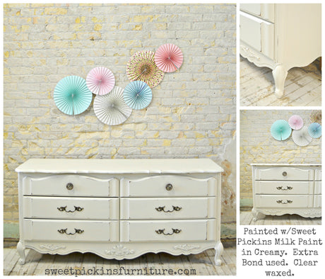 Antique white dresser painted in Old Fashioned Milk Paint’s Creamy color, set against a brick wall with pastel paper fans.