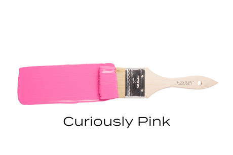 Paintbrush with CUREiously Pink Fusion Mineral Paint on bristles and handle, labeled below.