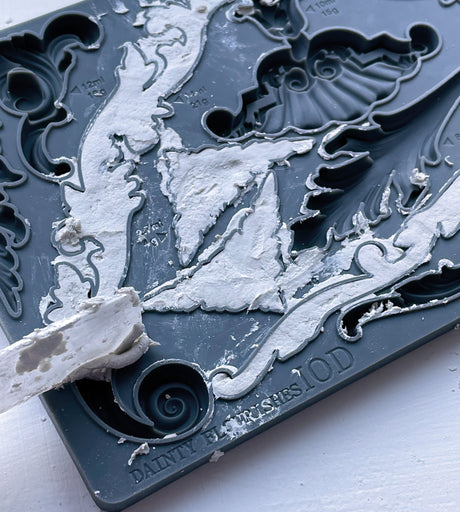 I.O.D. Dainty Flourishes Mould with white plaster in ornate designs; spatula partially visible.