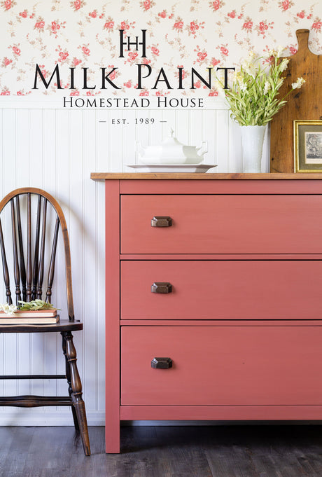 Pink dresser with 3 drawers in Homestead House Dala Red Milk Paint, topped with a vase of white flowers.