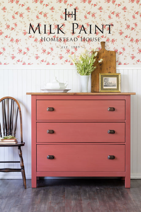 Dresser painted in Dala Red Milk Paint by Homestead House, shown near books and a chair.