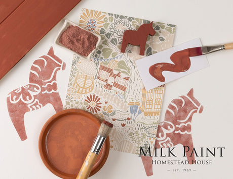 Brushes and painted horse figure with Homestead House Dala Red Milk Paint on floral backdrop labeled “Milk Paint”.