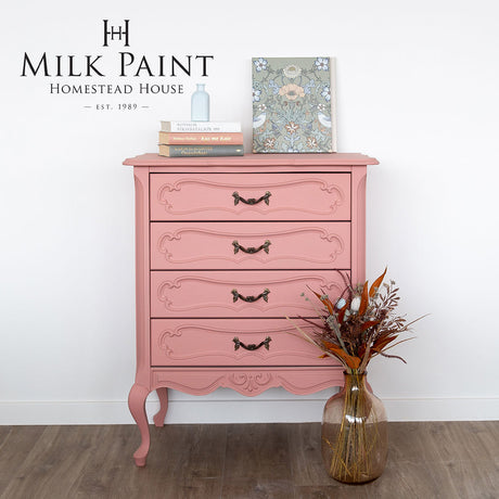 Pink dresser painted with Homestead House Dusty Rose Milk Paint, styled with books, art, and a vase with dried flowers.