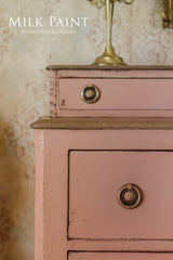 Dresser in Dusty Rose Milk Paint by Homestead House with ornate knobs and a lamp.
