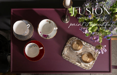 Three teacups on a maroon table painted with Fusion Mineral Paint in Elderberry, next to flowers and sugar bowls.