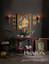 Purple table painted in Fusion Mineral Paint’s Elderberry, beside a black chair, candles, and vintage art.