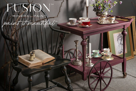 Tea cart in Fusion Mineral Paint’s Elderberry with teacups, silverware, and a portrait next to a black chair.