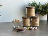 Candy eggs spill from glass jars on wood beside plants and the Emblems Mini-Stamp by I.O.D.