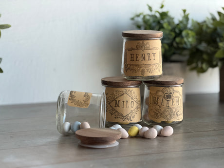 Candy eggs spill from glass jars on wood beside plants and the Emblems Mini-Stamp by I.O.D.