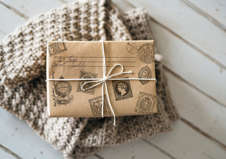 Brown paper package tied with string and I.O.D. Ephemeral Type Stamp on a folded knit blanket.