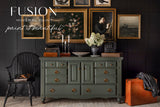 Everett Fusion Mineral Paint shown with gold accents, black chair, orange suitcase, and black wall.