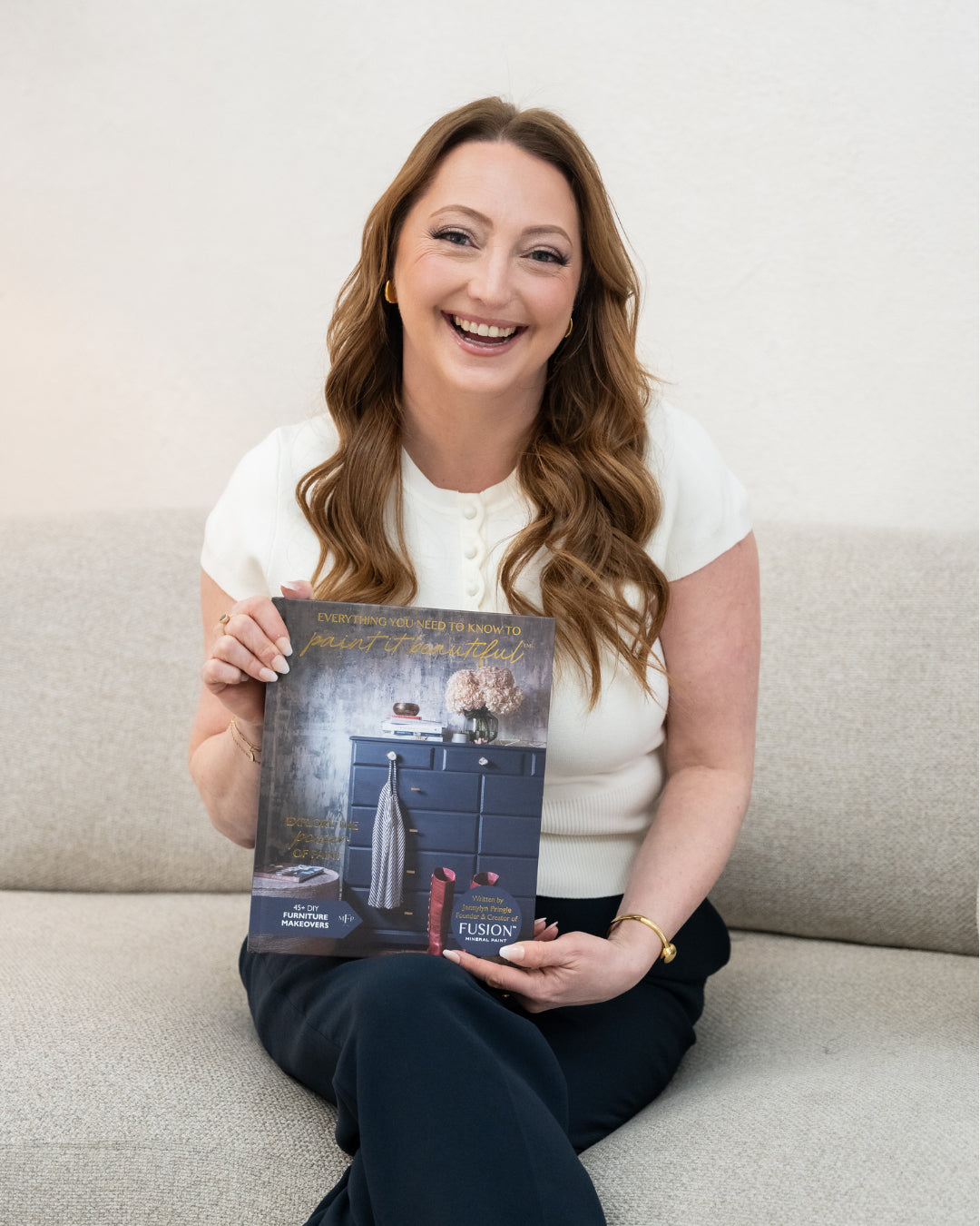 Woman on couch holding “Everything You Need to Know to Paint” book by Fusion Mineral Paint.