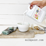 Hand pouring Sweet Pickins’ Extra Bond by Old Fashioned Milk Paint into a bowl, with paintbrush and cloth nearby.