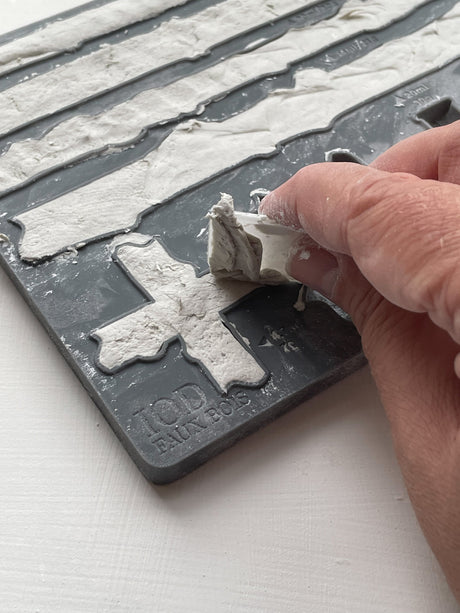 Hand holding a white clay plus sign from the I.O.D. Faux Bois Mould.