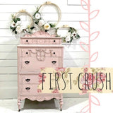 Pink vintage dresser painted with Old Fashioned Milk Paint, decorated with florals, embroidery hoops, and floral banner.