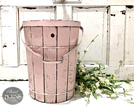 Pink metal bucket painted with First Crush by Old Fashioned Milk Paint near white flowers on rustic white wood.