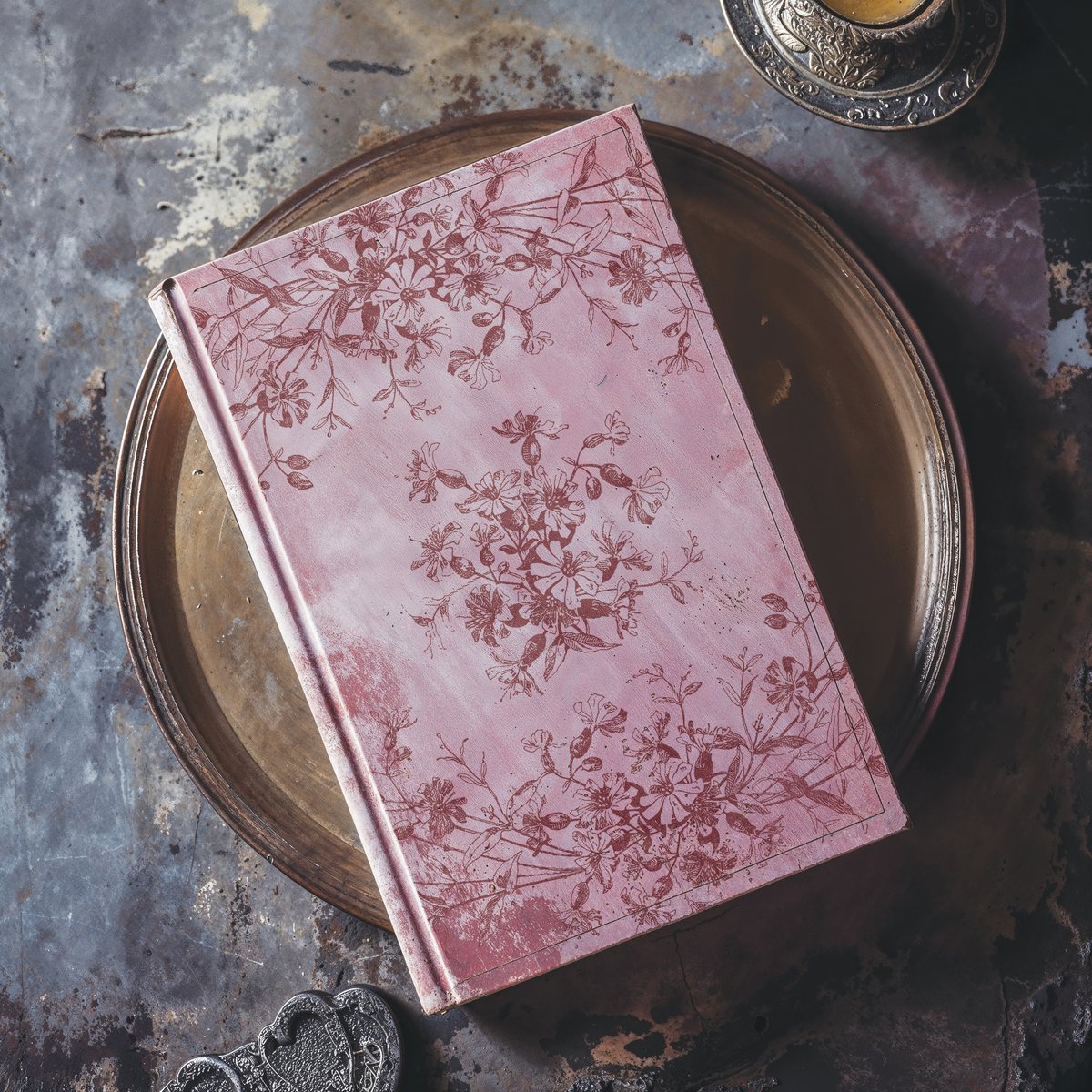 Pink floral book on iron tray, accented with Flora & Vine Stamp by I.O.D. and additional decorative items.