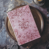 Pink floral book on iron tray, accented with Flora & Vine Stamp by I.O.D. and additional decorative items.