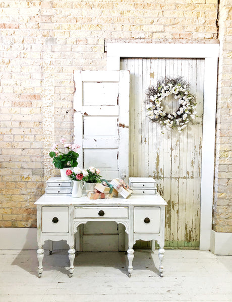 White desk painted in Old Fashioned Milk Paint Flour Sack, styled next to a rustic door with flowers and books.
