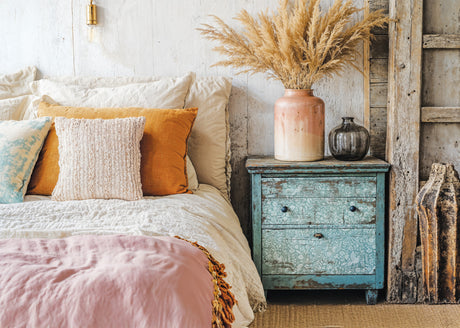 Bed with layered pillows, blanket, blue nightstand, and I.O.D. Folk Story Stamp folk art motifs.