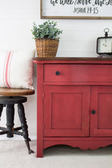 Red cabinet in Homestead House Fort York Red Milk Paint with black knob, greenery basket, pillow, and clock.