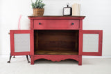 Red wooden cabinet in Fort York Red Milk Paint, doors open, with plant, books, and clock on top.