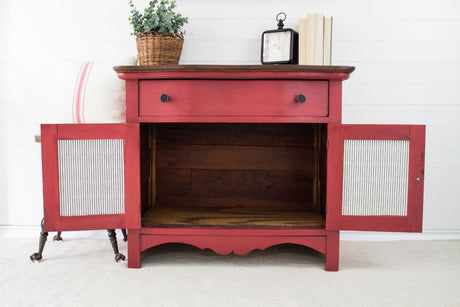 Red wooden cabinet in Fort York Red Milk Paint, doors open, with plant, books, and clock on top.