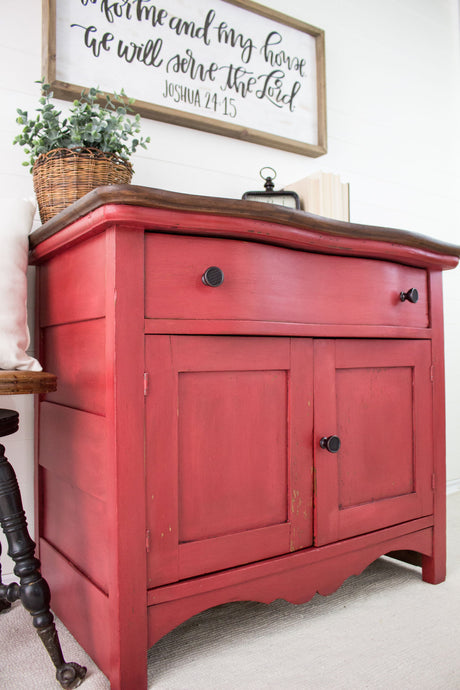 Cabinet painted in Homestead House Fort York Red Milk Paint beneath a Bible verse sign on a white wall.