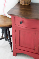 Homestead House Fort York Red Milk Paint on a wooden cabinet beside a vintage stool and wicker basket.