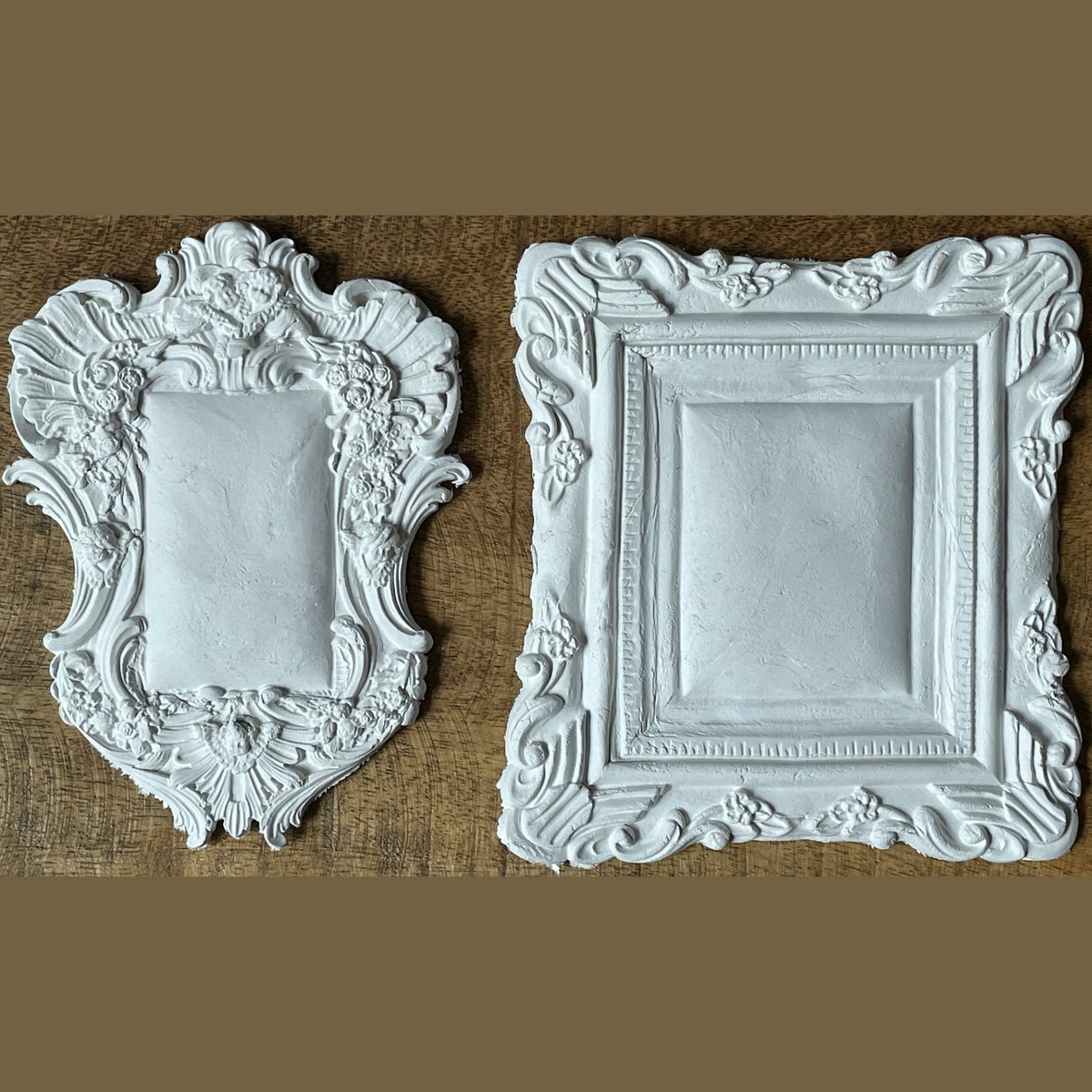 Two empty white Frames 2 Mould by IOD resting on wood, shown against a brown background.
