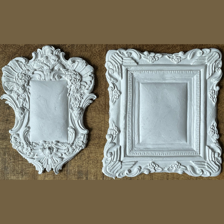 Two empty white Frames 2 Mould by IOD resting on wood, shown against a brown background.