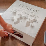 Hands opening Fusion Mineral Paint Briefcase Swatch Box Set labeled “True Colour Swatches” on a brown table.