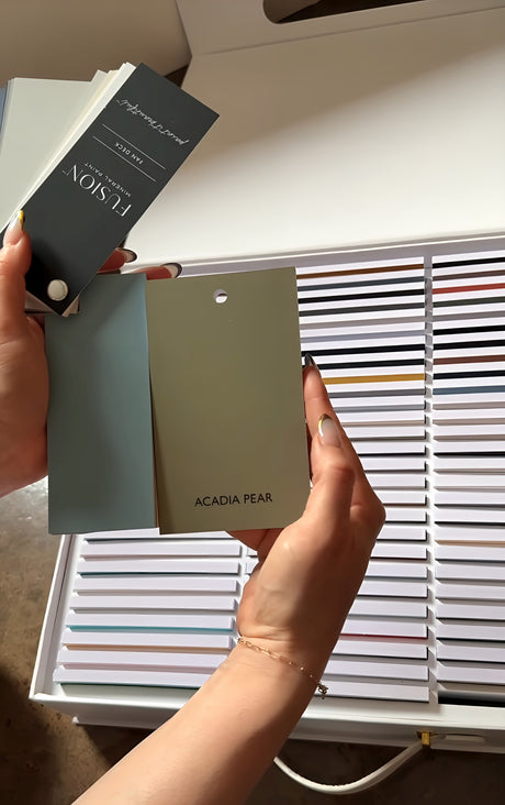 Hands hold Fusion Briefcase Swatch Box Set by Fusion Mineral Paint above an array of other color samples.