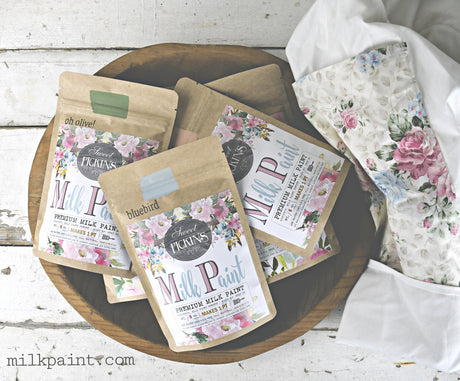Four Galvanized Sweet Pickins Milk Paint packets by Old Fashioned Milk Paint arranged in a wooden bowl.