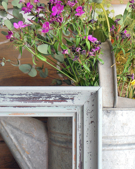 Purple flowers in a weathered can beside a distressed white frame painted with Galvanized by Old Fashioned Milk Paint.