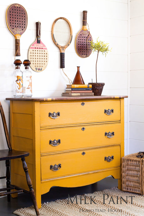 Dresser painted in Garden Seed Milk Paint by Homestead House, displayed beneath vintage rackets on a white wall.