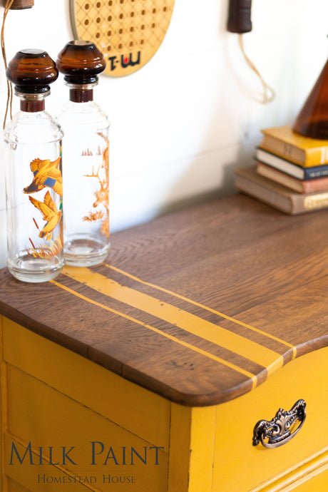 Two glass bottles with orange designs on a yellow Homestead House Garden Seed Milk Paint dresser.
