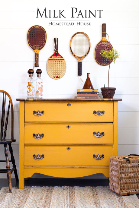 Yellow dresser in Homestead House Garden Seed Milk Paint with ornate pulls and vintage rackets on white shiplap.