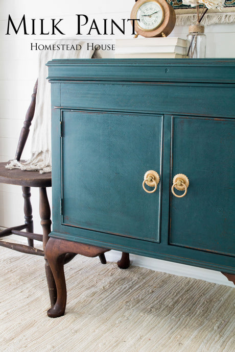 Cabinet painted in Gaspe Green Milk Paint by Homestead House on a beige rug with chair and decor nearby.