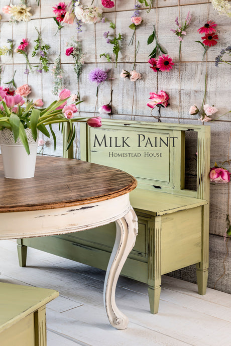 Homestead House Gatineau Milk Paint bench beside a wooden table, flowers displayed on a wood wall in background.