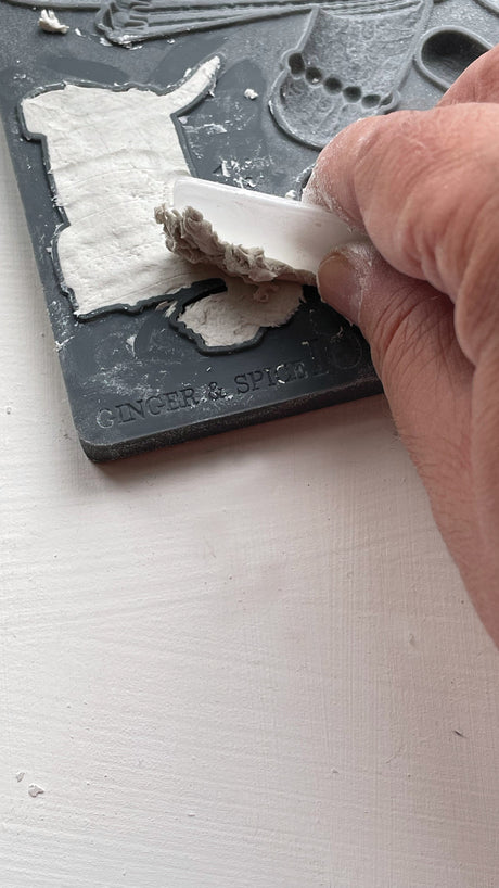 Hand pressing white clay into I.O.D. Ginger & Spice Mould (2023 Limited Release) on a gray surface.